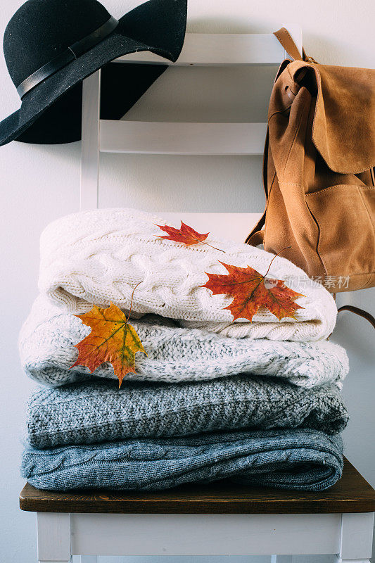 一堆暖和的衣服和秋叶放在椅子上。旅游的概念