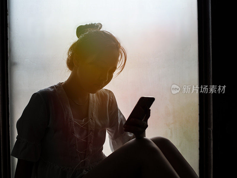 复古滤镜下的剪影，女孩正在用手机，坐在窗户上