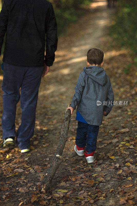 儿子拖着一根大树枝和父亲走在一起