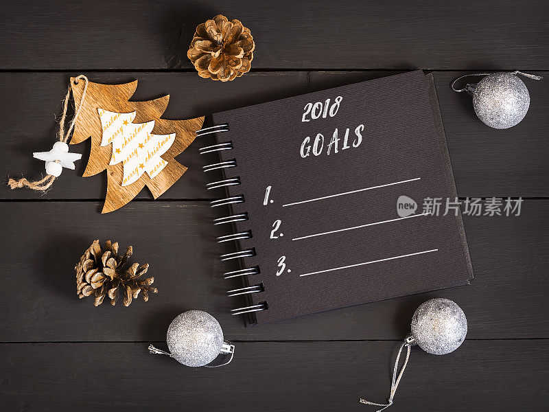 木桌上放着笔记本、圆锥体和圣诞装饰品，列出2018年目标清单。