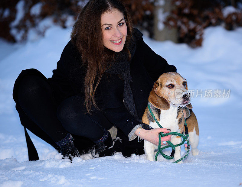 快乐的女人坐在雪和最好的朋友比格犬