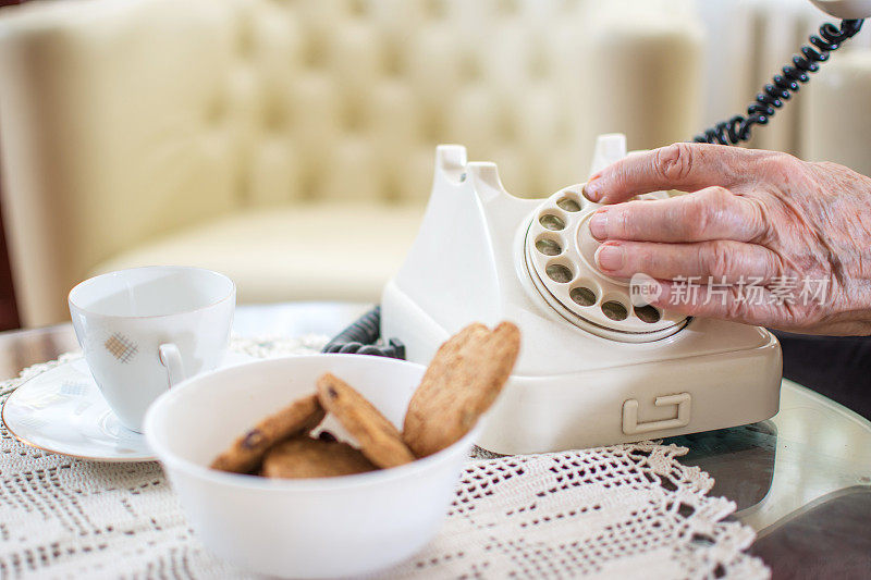 特写的年长妇女的手拨电话号码在复古座机在家里。