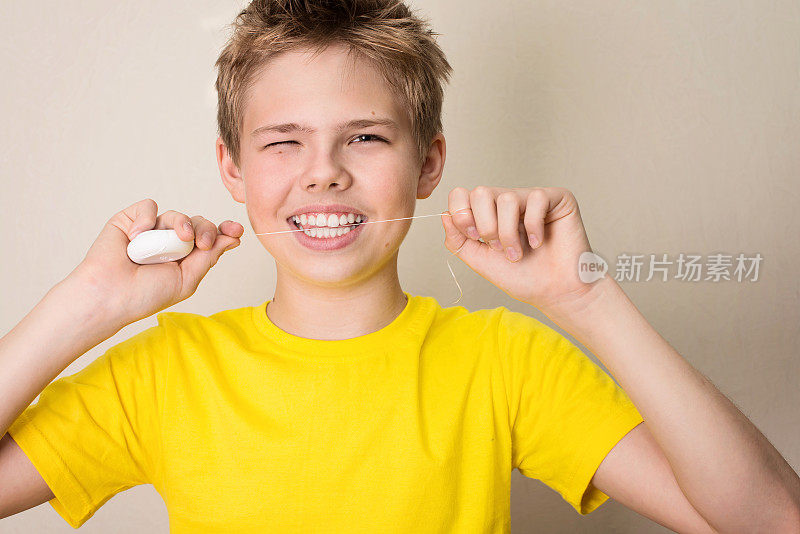 男孩用牙线清洁牙齿。特写的十几岁的男孩与牙线孤立。