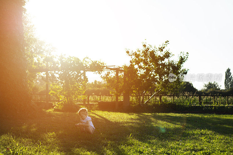 蹒跚学步的女孩坐在草地后院的乡村农舍
