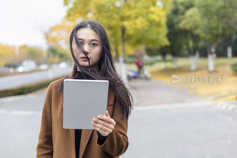 年轻的亚洲女子拿着平板电脑走在街上