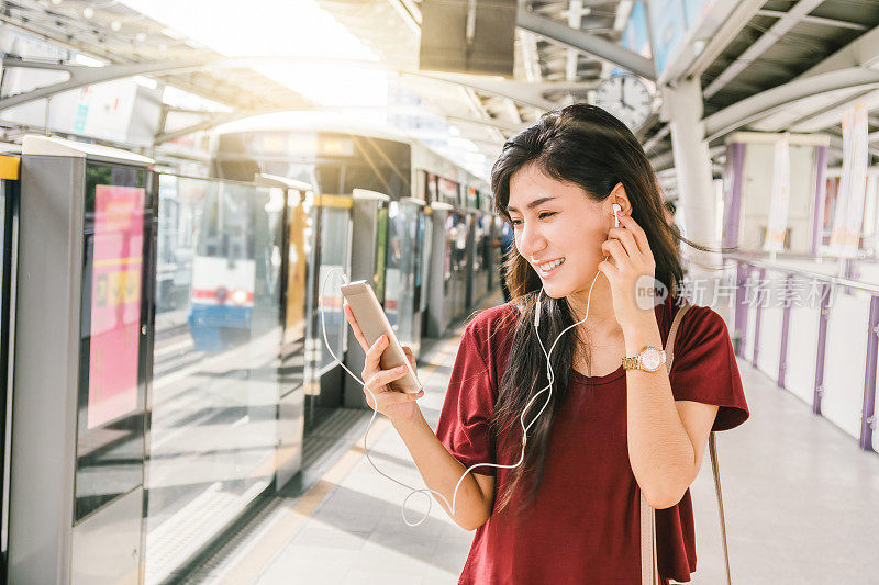 亚洲女性乘客穿着休闲服装，通过智能手机在BTS轻轨或捷运地铁上使用和听这首歌，在大城市旅行，生活方式和交通理念