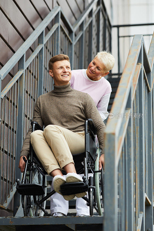 内容细心成熟的金发护士在户外扶着轮椅的残疾人下楼