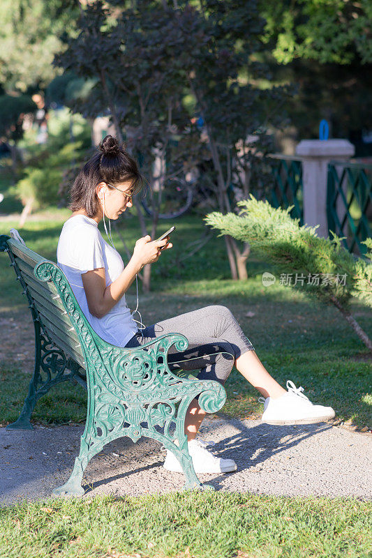 一个穿着运动服的年轻女子正在室外听手机里的音乐