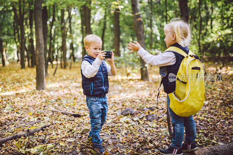 秋天的森林公园里，学龄前的孩子们用手机互相拍照。儿童爱好主题和积极的生活方式。专业的摄影师