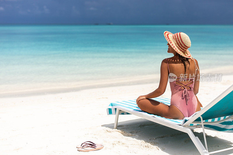 快乐的女人戴着太阳帽放松在沙滩的躺椅上。