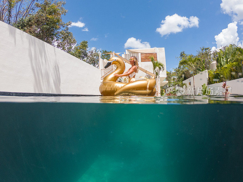 年轻女子在充气的金色天鹅在酒店游泳池里玩