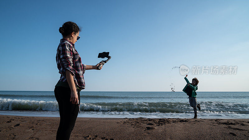年轻女子用智能手机在海滩上拍摄男孩