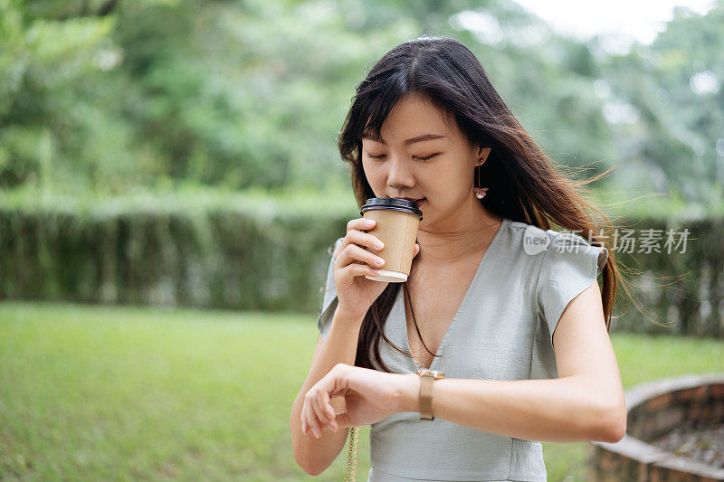 年轻时尚的亚洲女人喝外卖咖啡和检查时间