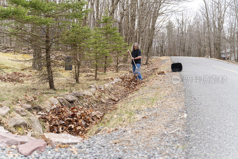 社区志愿服务。一名50岁的男子在春天清理路边的排水沟。