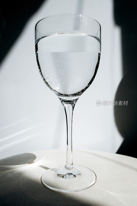 白底上的一杯水。玻璃反射强光。透明的酒杯。