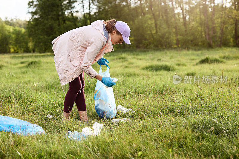 在日落时分，一个女人站在散落的布匹中间，拿着垃圾袋捡垃圾。环境污染理念，捡垃圾。