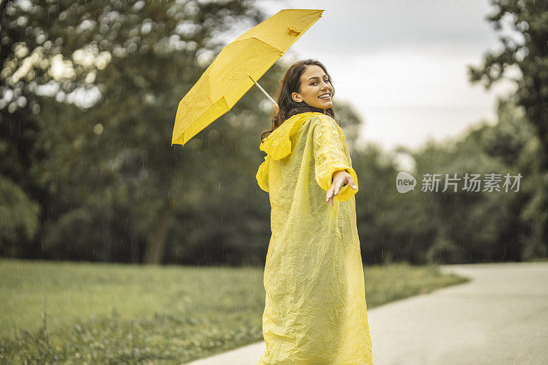拿着黄伞，穿着黄雨衣，享受着雨的女人