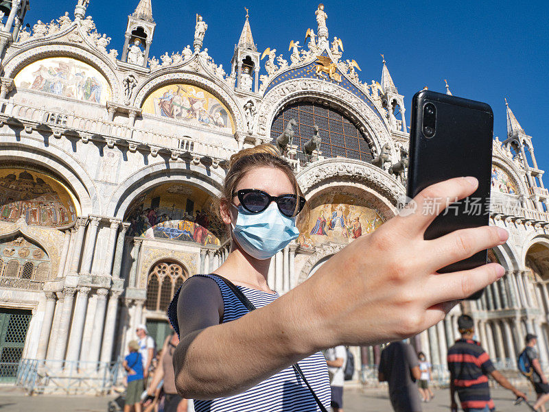 新冠肺炎大流行期间的一名游客。在圣马可广场，一名年轻女子戴着外科口罩，背景是圣马可大教堂。意大利著名的旅游胜地。