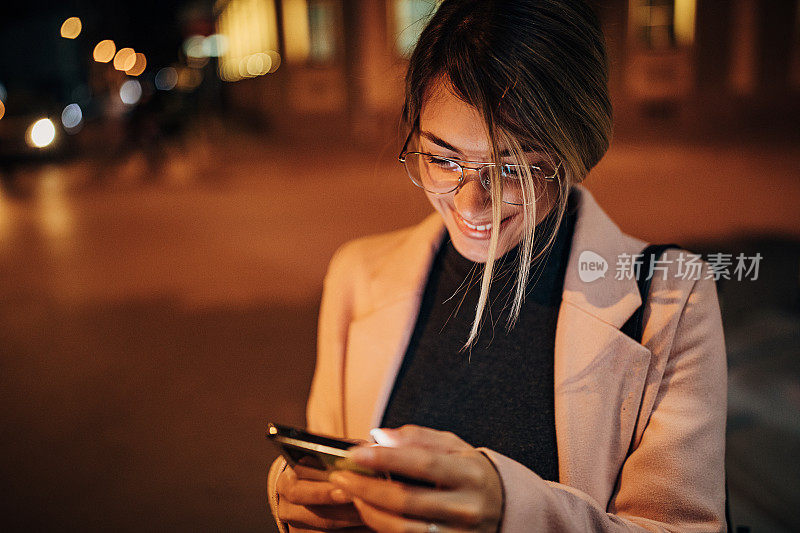 美丽快乐的女人晚上在城市的户外使用手机