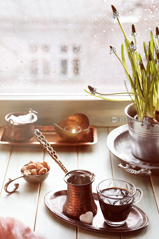 传统土耳其铜咖啡壶的东方咖啡，窗台上有花。木窗与风信子花盆。寒冷的春天雨天。舒适的场景，hygge概念