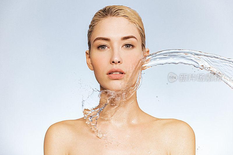 年轻女子的照片与清洁的皮肤和飞溅的水。金发女人的肖像，脸上有水滴。温泉治疗。女孩用水洗她的身体。水和身体。