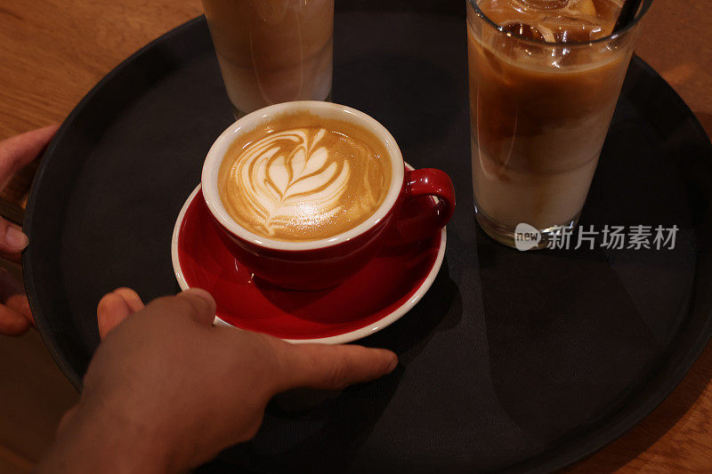咖啡师端上一杯牛奶泡沫上有花图案的拿铁