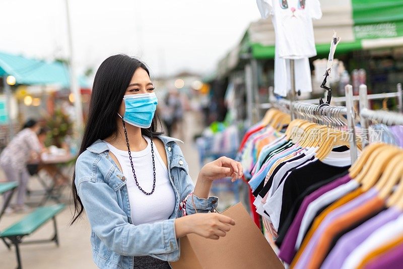 在泰国曼谷当地的夜市，一名戴着防护面膜的女性独自购物