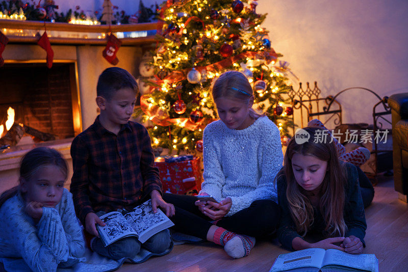 小孩子坐在圣诞树前读书，玩得很开心