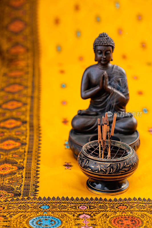 在一个金佛前的香碗里的熏香和刺绣的黄橙色印度教纱丽绳的特写