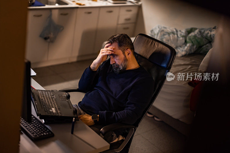疲惫的成熟商人晚上在家里用笔记本电脑工作，在家庭办公室工作