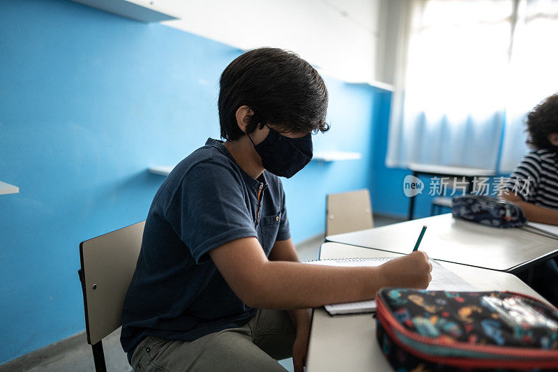 男孩在课堂上学习，戴着防护口罩