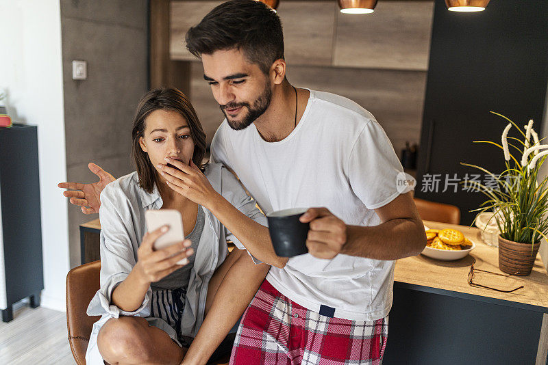 可爱幸福的夫妇看着厨房里的手机