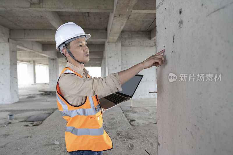 一位男性工程师在一座现代化办公楼的建筑工地用笔记本电脑工作。