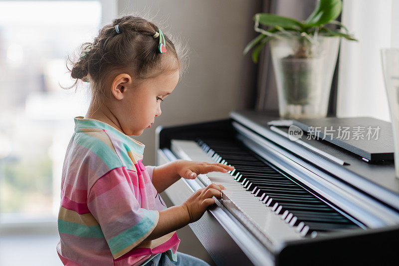 可爱的亚洲女孩在家里弹钢琴的侧面视图