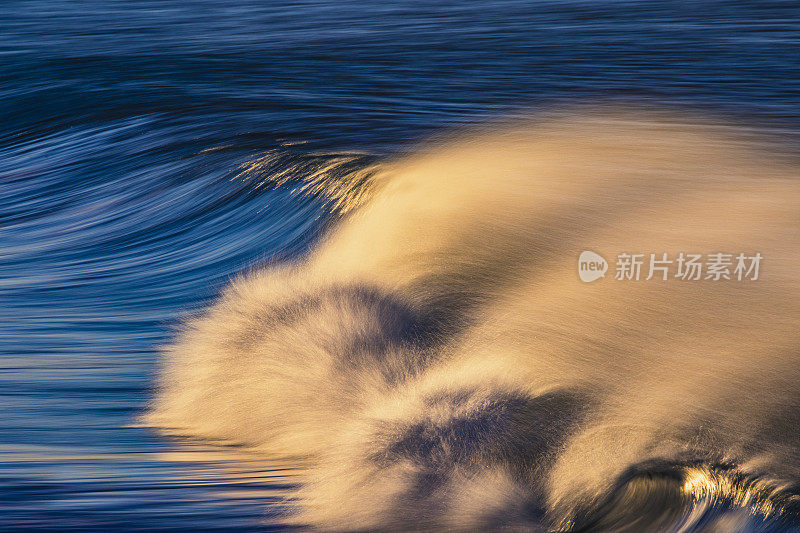 干净的海浪打破反射在海滩上明亮的金色日出的特写