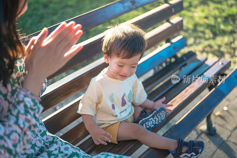 小男孩和妈妈坐在公园的长椅上欣赏日落