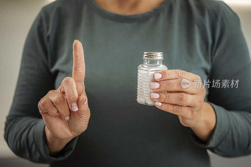 女人拿着盐瓶，用手指做手势