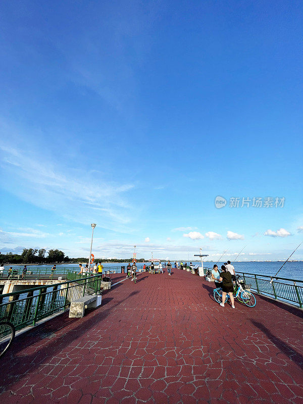 新加坡东海岸公园码头上的自行车手和渔民，绿色的栏杆，多云晴朗的蓝天