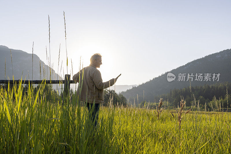 牧场主在木栅栏旁休息时使用数字平板电脑