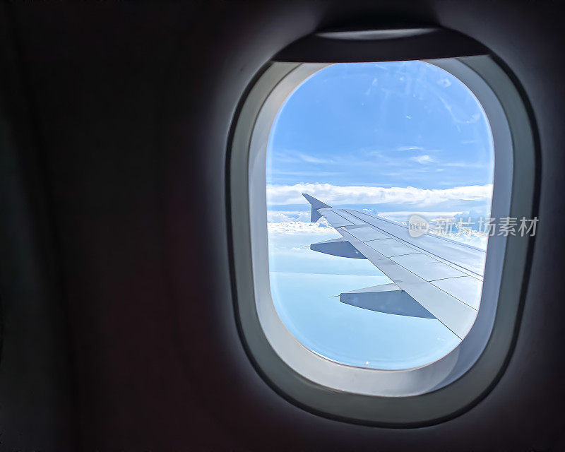 透过窗户看飞机在机翼飞行，有一个美丽的蓝天和岛屿。飞机窗外的景色。白天阳光灿烂的白天。