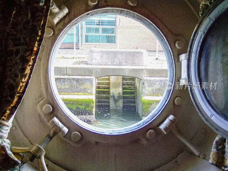 一艘非常古老的船打开的舷窗，望向船坞墙。