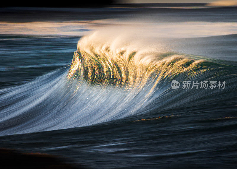 缓慢的快门模糊的平滑波浪打破礁石在海洋与戏剧性的金色光