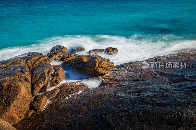 慢快门海岸场景，海水蓝色的海浪轻轻地冲刷着岩石