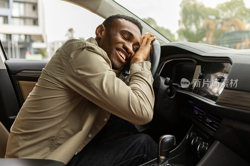 高兴的非洲裔美国人拥抱着他的新车方向盘，闭上眼睛微笑着