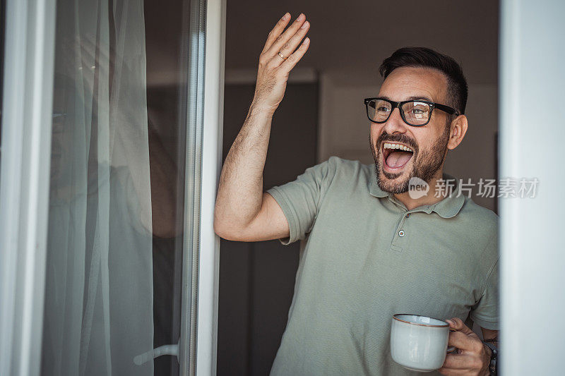 一位成年男子端着一杯咖啡，面带微笑地站在公寓的阳台门口