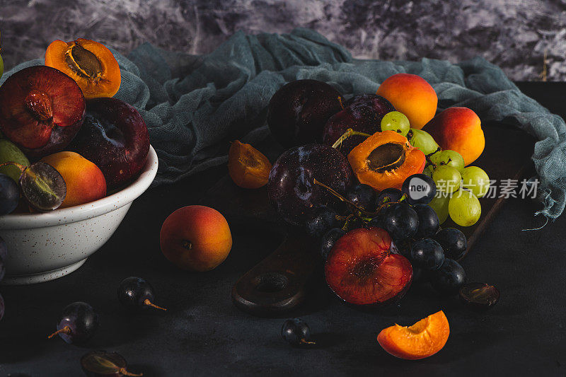 刚洗过的有水滴的水果。明亮的高基调外观传达新鲜感。各种新鲜葡萄，杏和羽毛在深色背景。维生素的水果来源