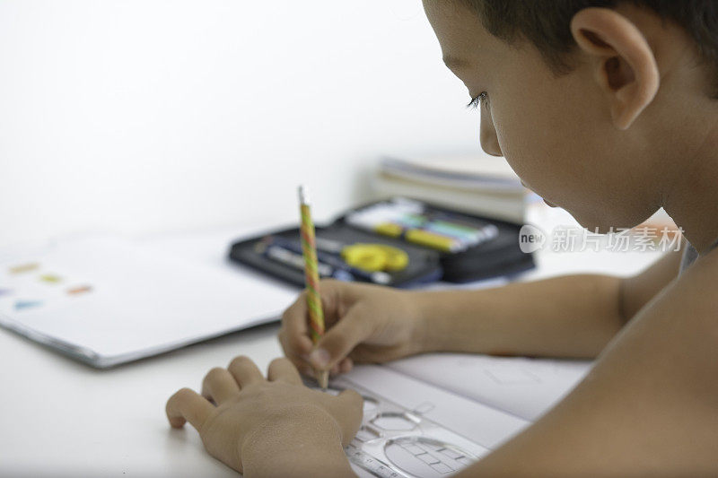 漂亮的男孩坐在桌子旁做他的学校作业