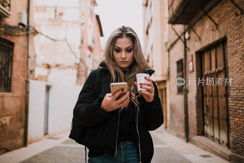 年轻女子拿着外带咖啡杯看着智能手机