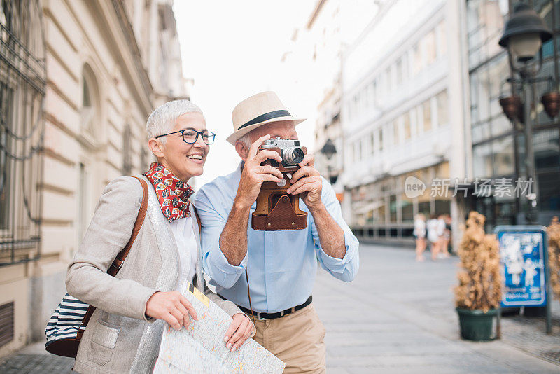 微笑的女人拿着地图站在年长的男人旁边用相机拍照
