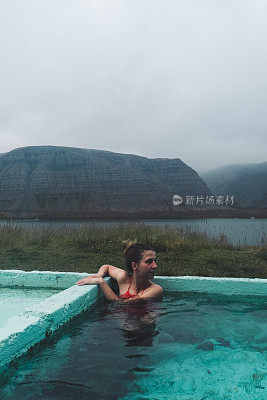 在冰岛的峡湾景色中，一个女人在热水池里洗澡